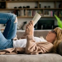 Eine junge Frau liegt lesend auf einem Sofa. 