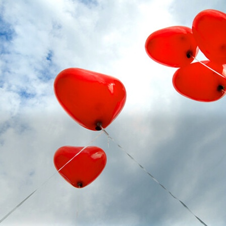 Mehrere Herzluftballons fliegen vor blauem Himmel.