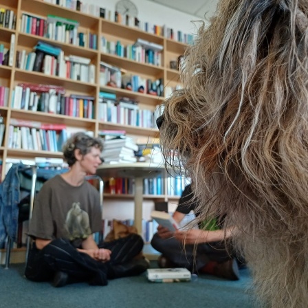 Ein Hund und eine Frau sitzen auf dem Boden vor einem Bücherregal. 