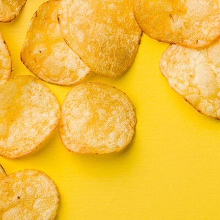 Eine Handvoll Kartoffelchips liegen auf einem gelben Tisch.