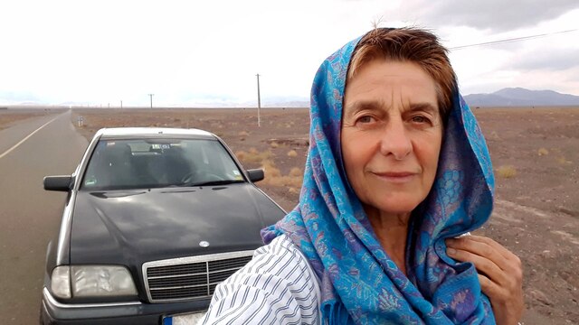 Ältere Frau mit Kopftuch vor ihrem Auto