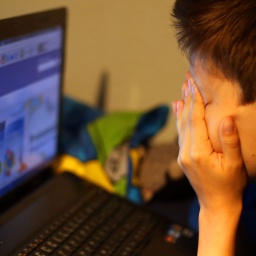 Ein Junge sitzt vor einem Computer und reibt sich die Augen.