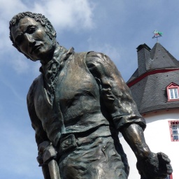Das Foto zeigt den sogenannten Schinderhannes als Metallskulptur. Im Hintergrund ist ein weißer Turm zu sehen. 