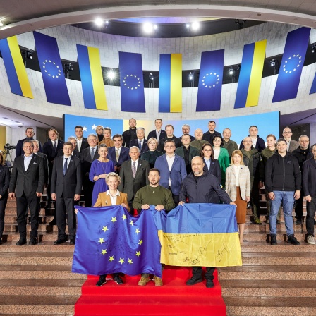 Wolodymyr Selenskyj (vorne Mitte), Präsident der Ukraine, Ursula von der Leyen (vorne l.), Präsidentin der EU-Kommission, und Denys Schmyhal (vorne r.), Ministerpräsident der Ukraine, halten eine europäische und eine ukrainische Fahne während eines Gruppenfotos nach dem EU-Ukraine-Gipfel im Februar. (Bild: dpa / Ukraine Presidency)