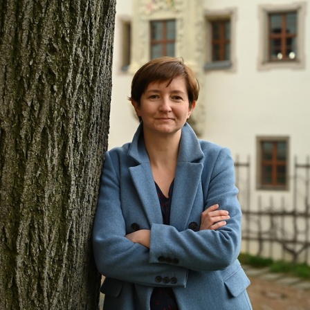 Eine Frau in blauer Jacke lehnt an einem Baum
