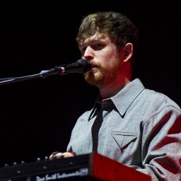 Der Musiker James Blake in hellgrauem Hemd sitzt an Keyboard und Mikrofon.