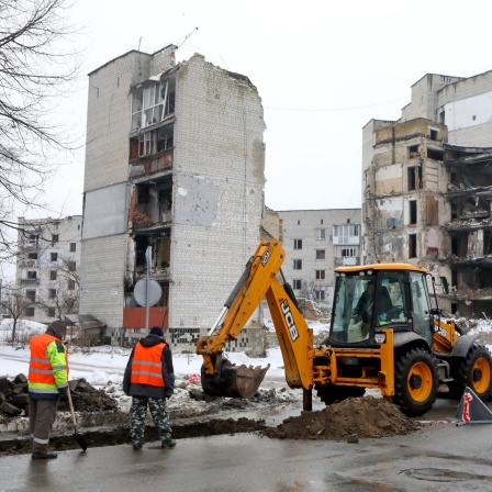 Mitarbeiter eines Versorgungsunternehmens arbeiten vor einem durch russischen Beschuss zerstörten mehrstöckigen Gebäude in der Tsentralna-Straße im Norden der Zentralukraine.