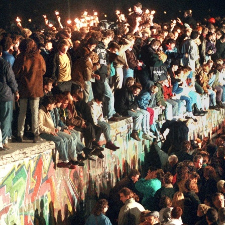 Jubelnde Menschen sitzen mit Wunderkerzen auf der Berliner Mauer am 11.11.1989.