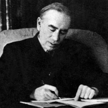Der Ökonom John Maynard Keynes sitzt an einem Schreibtisch und blickt auf Unterlagen