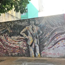 Ein Wand-Graffiti in Buenos Aires auf einer Mauer stellt den Musiker Carlos Gardel dar, davor steht ein Baum