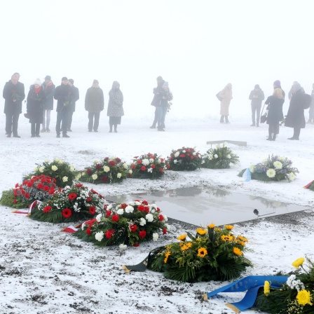 Teilnehmer stehen im Nebel bei einer Kranzniederlegung im ehemaligen Konzentrationslager Buchenwald vor Kränzen an einer Gedenkplatte. Der international begangene Holocaust-Gedenktag am 27. Januar erinnert an die Befreiung des deutschen Vernichtungslagers Auschwitz 1945.