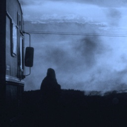 Die Silhouette einer Person steht bei wolkigem Himmel vor einem Wohnwagen