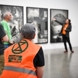 Führung im Musem Folkwang, im Vordergrund ist eine Person mit knalloranger "Extiction Rebellion"-Weste zu sehen, im Hintergrund eine Person, die ein Bild in der Ausstellung erläutert.