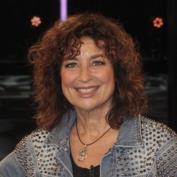 Schauspielerin Isabel Varell sitzt in einer Jeansjacke auf einem Stuhl und lacht in die Kamera.