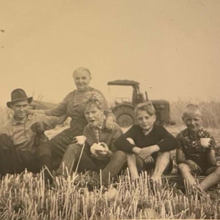 Gruppe von Menschen posiert nach getaner Feldarbeit für ein Erinnerungsfoto, Schwarz-weiß-Bild aus der Zeit nach dem Zweiten Weltkrieg