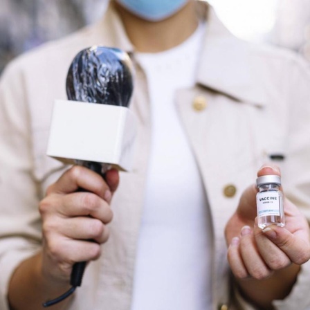 Eine Reporterin hält eine Impfdosis in die Kamera