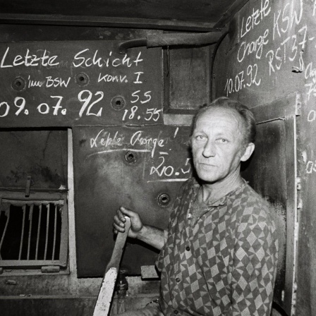 Ein Arbeiter blickt besorgt in die Kamera. Die schwarz-weiße Aufnahme ist entstanden im Stahl- und Walzwerk Maxhütte in Unterwellenborn, Thüringen, nach der letzten Schicht im Juli 1992. 