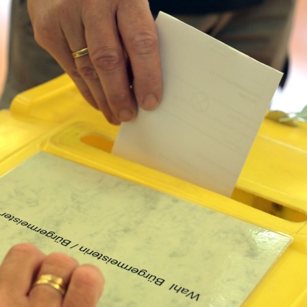 Eine Frau steckt einen Wahlumschlag in die Urne