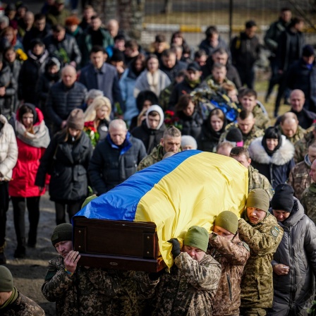 Sodaten tragen einen mit ukrainischer Flagge bedeckten Sarg, gefolgt von Trauernden