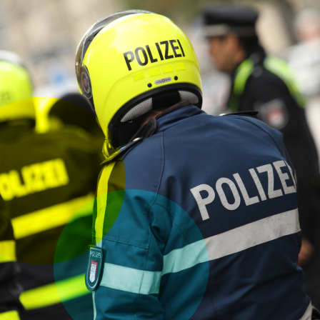 Eine Gruppe von Polizeibeamten. Im Hintergrund sind verschwommene Umrisse weiterer Personen und Verkehrselemente