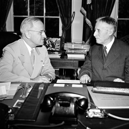 US-Präsident Harry Truman (linkts) nach seiner Rückkehr von der Potsdamer Konferenz an seinem Schreibtisch im Weißen Haus mit Kriegsminister Henry L. Stimson. Die Männer diskutieren über die Atombombe, die auf die japanische Stadt Hiroshima abgeworfen wurde.