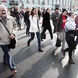 Etwa zehn Menschen überqueren zielstrebig die Straße. Sie scheinen sich fremd zu sein. Im Hintergrund sieht man Häuser, Autos und weitere Passanten.
