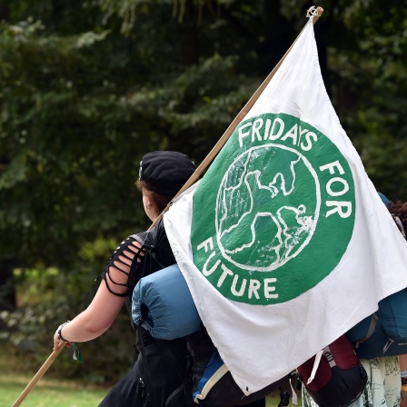 Eine Teilnehmerin des Sommerkongresses der Fridays for Future Bewegung trägt eine Fahne mit dem Logo der Bewegung