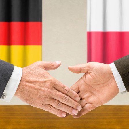 Zwei Männer reichen sich die Hand. Im Hintergrund sind eine Deutschland- und eine Polenfahne zu sehen (Bild: Zerbor/Shotshop/picture alliance)