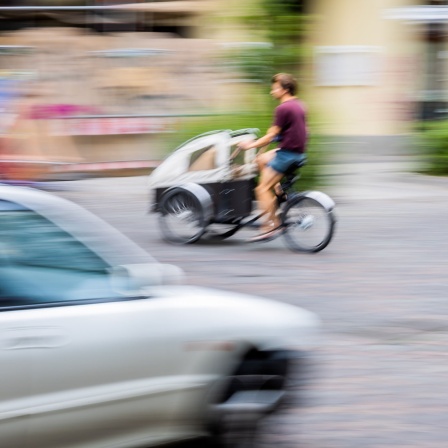Eine Person fährt mit einem Lastenrad im Graefekiez im Berliner Stadtteil Kreuzberg an einem Auto vorbei. © dpa/Christoph Soeder