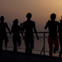 Eine Gruppe von Menschen in schnellem Lauf an einer Meerespromenade bei Sonnenuntergang.