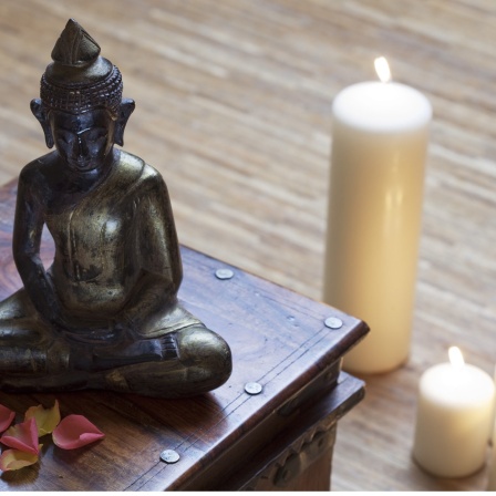 Eine Buddhafigur sitzt auf einer Holzschachtel, daneben brennen Kerzen