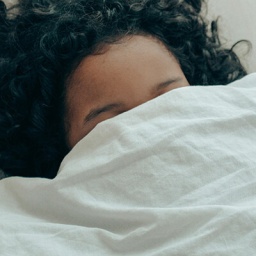 Eine junge Frau hat sich die Bettdecke übers Gesicht gezogen.