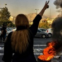 Eine Frau steht während einer Demonstration in Teheran vor einem brennenden Autoreifen und zeigt das Victory-Zeichen.