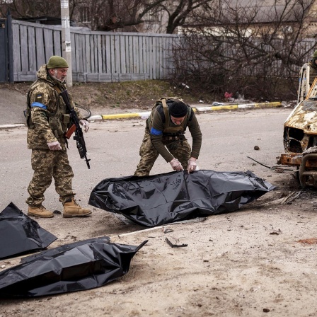 Zwei ukrainische Soldaten bergen die Überreste von vier getöteten Zivilisten aus einem verkohlten Fahrzeug in Butscha.