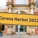 Ein symbolisches gelbes Hinweisschild mit der Aufschrift &#034; Corona Herbst 2022&#034; vor dem Robert-Koch-Institut (RKI) in Berlin-Wedding. Als Bundesoberbehörde spielt das RKI eine wichtige Rolle bei der fortdauernden Erfassung der aktuellen Lage der Ausbreitung von COVID-19.