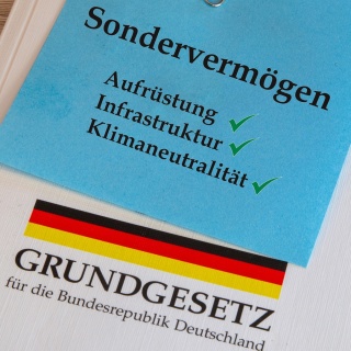 Das Deutsche Grundgesetz mit einem angehefteten Notizzettel mit der Aufschrift Sondervermögen, Aufrüstung, Infrastruktur und Klimaneutralität.  