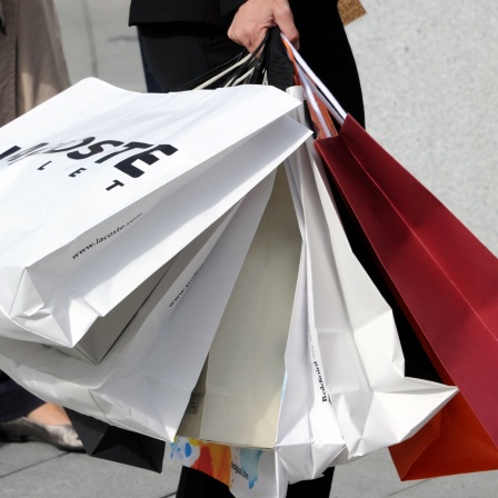 Eine Frau trägt mit einer Hand mehrere Einkaufstragetaschen mit Modeartikeln