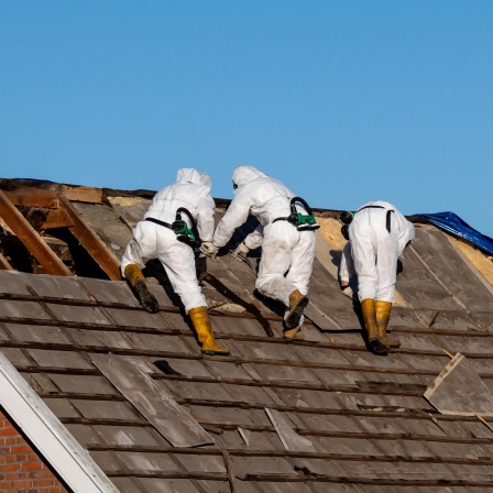 Fachleute in Schutzanzügen entfernen Asbestzement-Dachplatten.