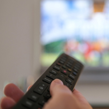 Eine Hand bedient eine Fernbedienung für ein TV-Gerät.