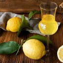 Ein Limoncello steht auf einem Tisch, im Hintergrund Zitronen