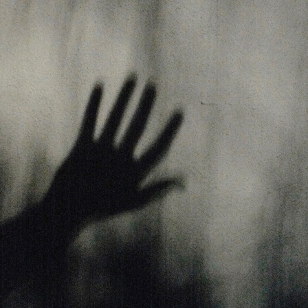 Körnige schwarzweiß Fotografie einer Hand hinter einer milchigen Glasscheibe