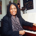Die amerikanische Sängerin Abbey Lincoln sitzt vor einem Klavier und lächelt.
