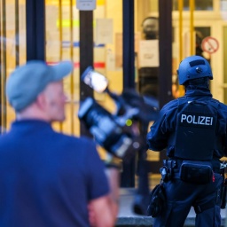 Im Fokus ist ein Polizist, verschwommen im Vordergrund ist ein Kameramann zu sehen.