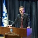 Israelischer Außenminister Eli Cohen hält eine Fahne, seitlich sind die Landesflaggen aufgestellt