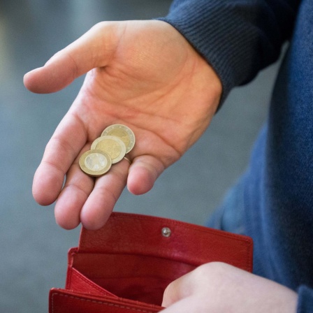 Münzen im Wert von fünf Euro werden über ein rotes Portemonnaie gehalten. 
