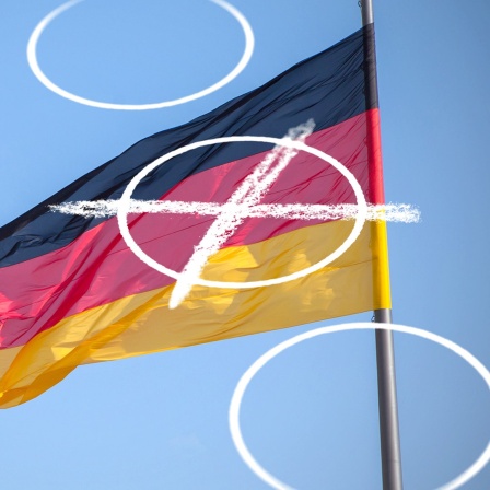 Eine Deutschlandflagge weht hinter einem Wahlkreuz vor dem Bundestag.