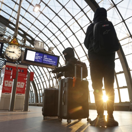 Menschen mit Koffern warten auf einem Bahnsteig am Hauptbahnhof in Berlin, Deutschland.