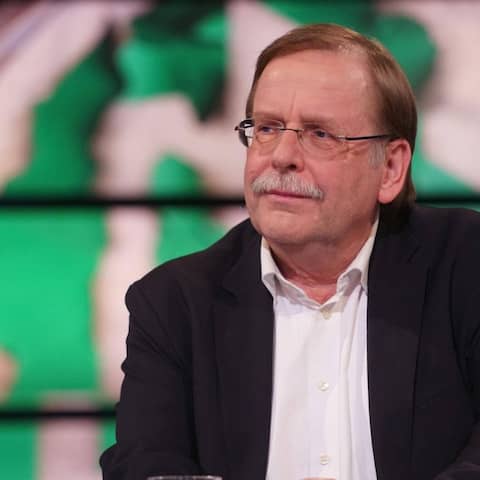 Rainer Koch sitzt vor einer Grafik eines verschwommenen DFB-Wappens.