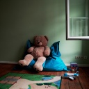 Ein großer Teddy sitzt auf einem Sitzsack in einem Spielzimmer. Daneben liegen weitere Spielsachen.