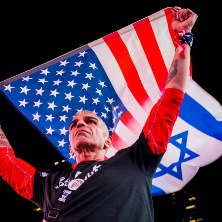 Ein Mann hält eine Flagge USA/Israel hoch (Foto:IMAGO / ZUMA Press Wire)